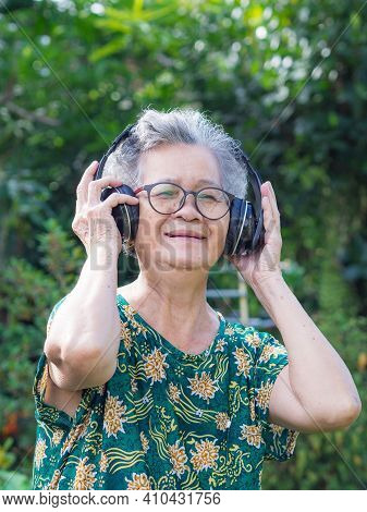 Senior Woman With Short Gray Hair Wearing Wireless Headphones Listening To A Favorite Song, Smiling 