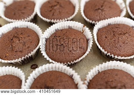 Brown Chocolate Muffins Wrapped In White Paper Baked In The Oven, Lying On Baking Paper.