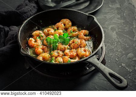 Shrimps with garlic, olive oil and parsley in frypan on black background