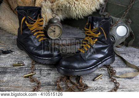 Leather Boots With Rusted Chains And Bullet Shells With Military Gas Mask And Fur Coat In Background