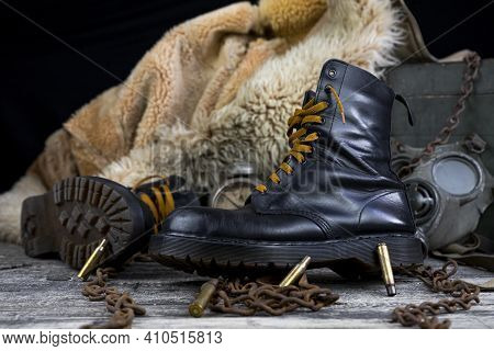 Leather Boots With Rusted Chains And Bullet Shells With Military Gas Mask And Fur Coat In Background