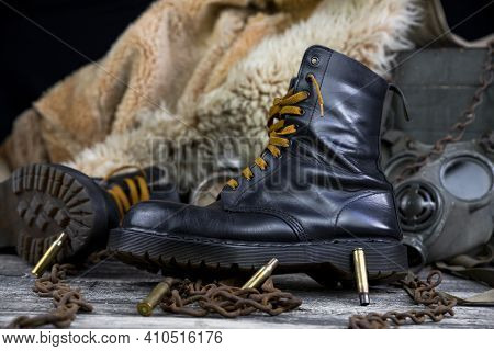 Leather Boots With Rusted Chains And Bullet Shells With Military Gas Mask And Fur Coat In Background