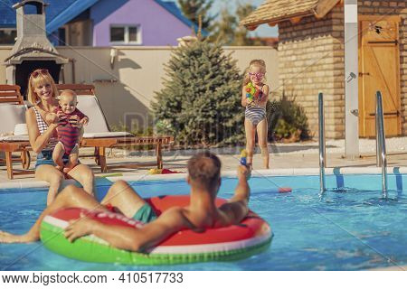 Cheerful Parents Having Fun Playing With Their Children With Squirt Guns By The Swimming Pool Splash