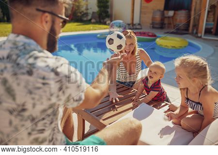 Mother And Father Having Fun Playing With Their Children On A Sun Bed By The Swimming Pool, Relaxing