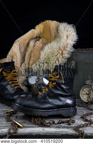 Leather Boots With Rusted Chains And Bullet Shells With Military Gas Mask And Fur Coat In Background