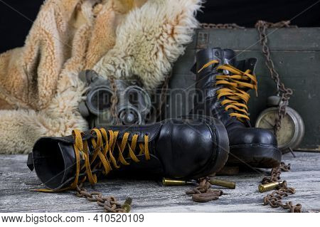 Leather Boots With Rusted Chains And Bullet Shells With Military Gas Mask And Fur Coat In Background
