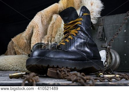 Leather Boot With Rusted Chains And Bullet Shells With Military Gas Mask And Fur Coat In Background