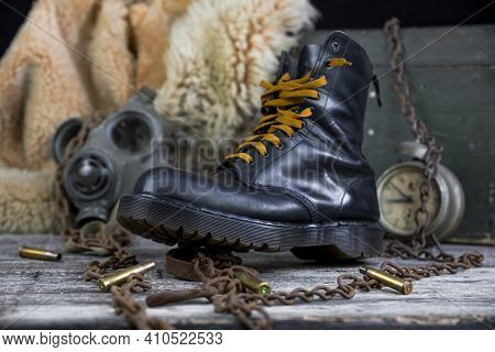 Leather Boot With Rusted Chains And Bullet Shells With Military Gas Mask And Fur Coat In Background
