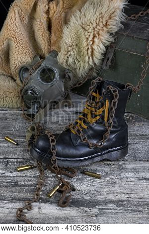 Leather Boot With Rusted Chains And Bullet Shells With Military Gas Mask And Fur Coat In Background