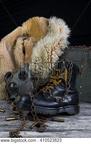 Leather Boot With Rusted Chains And Bullet Shells With Military Gas Mask And Fur Coat In Background