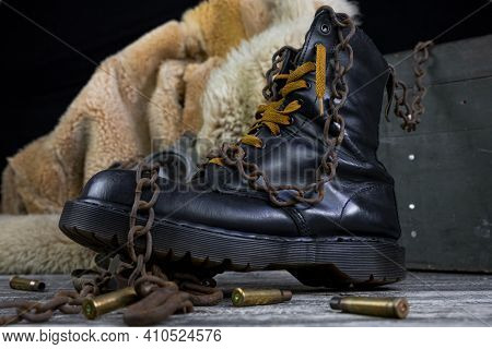 Leather Boot With Rusted Chains And Bullet Shells With Military Gas Mask And Fur Coat In Background