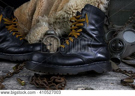 Leather Boots With Rusted Chains And Bullet Shells With Military Gas Mask And Fur Coat In Background