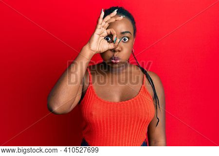 Young african american woman doing ok sign on eye puffing cheeks with funny face. mouth inflated with air, catching air. 