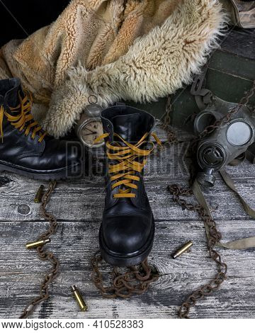Leather Boots With Rusted Chains And Bullet Shells With Military Gas Mask And Fur Coat In Background