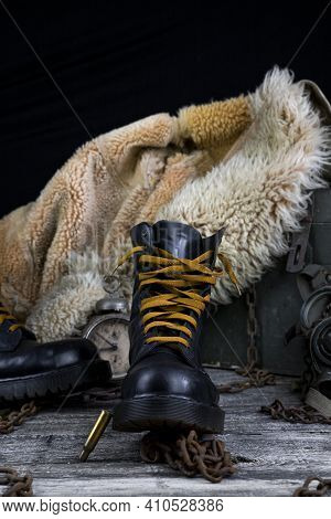 Leather Boot With Rusted Chains And Bullet Shells With Military Gas Mask And Fur Coat In Background