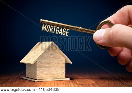 Key To Your Own Home Is To Get Mortgage. Wooden Model Of House And Key With Text Mortgage In Hand.