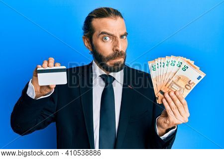 Attractive business man with long hair and beard holding credit card and euros skeptic and nervous, frowning upset because of problem. negative person. 