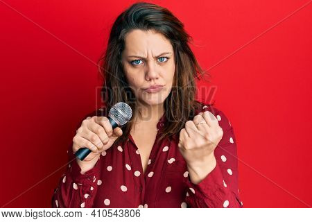 Young caucasian woman singing song using microphone annoyed and frustrated shouting with anger, yelling crazy with anger and hand raised 