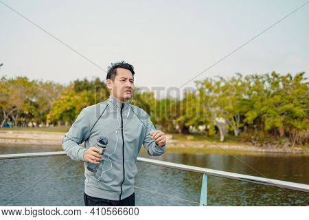 Young Sport Man Hold Water Bottle Between Jogging And Listening Music In The Park.