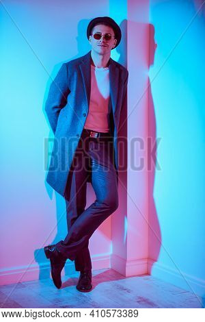 Full length porttrait of a handsome middle-aged man in an elegant coat and a hat standing by a white wall and smiling. Men's beauty, fashion. Lifestyle. Hipster man. 