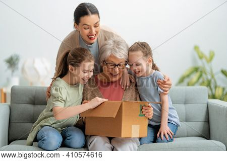 Grandmother, her daughter and granddaughters are unpacking cardboard box at home.