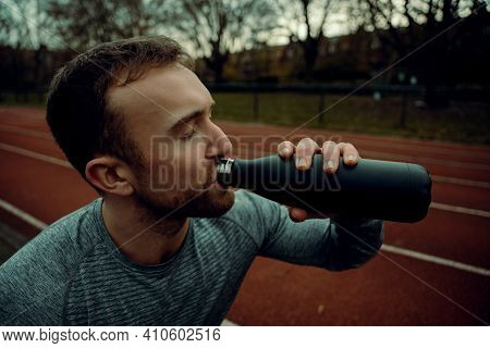 Caucasian Male Athlete Standing On Tracking Field Drinking Watr From Bottle
