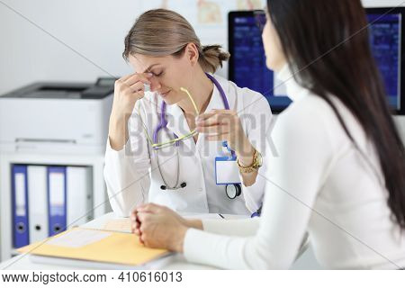 Tired Doctor Taking Off Glasses In Front Of Patient In Clinic. Medical Bad News Concept