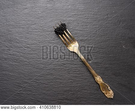 Fresh Grainy Black Paddlefish Caviar In Metal Fork On A Black Background, Top View
