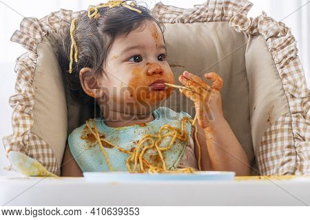 Adorable Little Child Funny Girl Eating Spaghetti With Spoon While Sitting In High-powered Chair At 