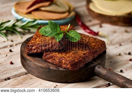 closeup of some tofu fillets on a dark wooden tray on a white rustic table, next to some cold cuts made of tofu and some slices of vegan cheese, in different plates