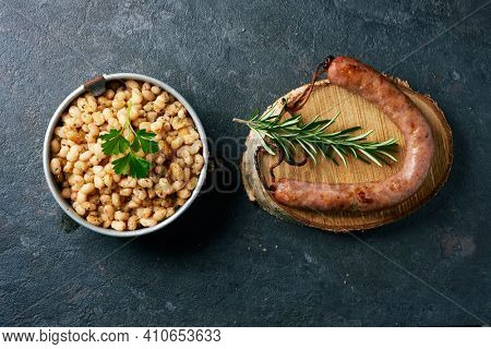 high angle view of botifarra amb mongetes, literally sausage and white beans, a dish traditional of catalonia, spain, served in an old metallic lunch box and a wooden plate, on a slate stone surface
