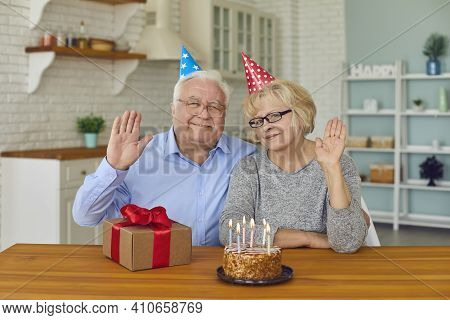 Happy Retired Couple In Festive Hats Sitting With Birthday Cake And Present Box
