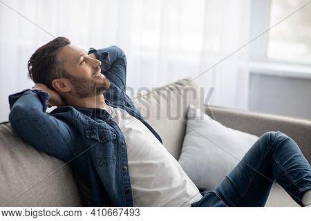 Closeup Of Carefree Bearded Man In Casual Clothes Relaxing On Couch At Home, Looking At Copy Space, 