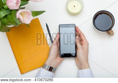 Women's Hands Holding Up-to-date Smartphone, White Background. Coffee Break Top View. Women's Busine