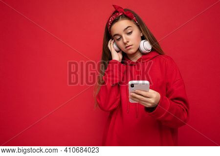 Photo Of Beautiful Concentrated Brunette Girl Wearing Red Hoodie Isolated On Red Background Holding 