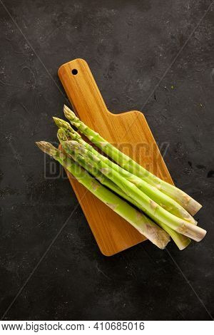 Bunch Of Asparagus On Wooden Cutting Board On Dark Gray And White Background.