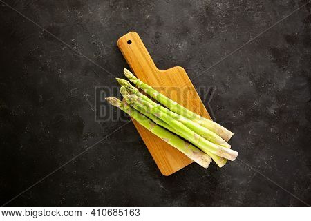 Bunch Of Asparagus On Wooden Cutting Board On Dark Gray And White Background.