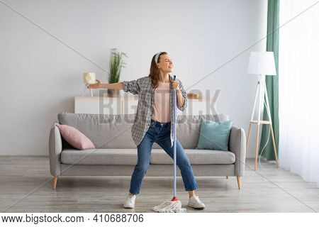 House Cleaning With Fun. Happy Housewife Singing Her Favorite Song During Cleanup, Using Mop As Micr