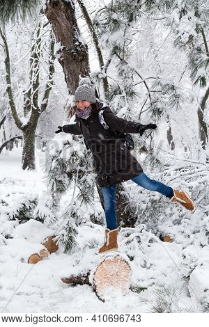 Smiling Young Woman Standing On Fallen Tree After Sleet Load And Snow In A Snow-covered Winter Park.
