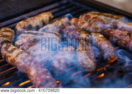 Preparing Meat Rolls Called Mici Or Mititei On Barbecue. Close Up Of Grill With Burning Fire With Fl