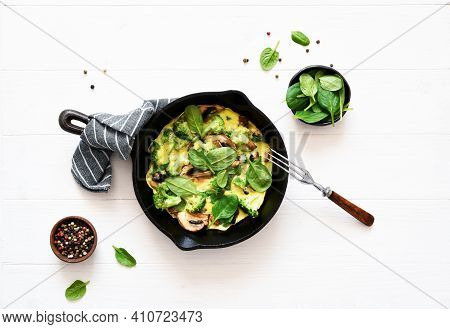 Omelet With Spinach And Mushrooms In A Cast-iron Pan On A Light Wood Background. Fritata With Spinac