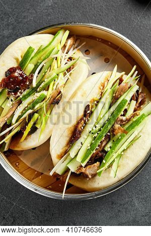 Bao bun with roast duck. Bamboo steamer on dark slate table. Chinese, asian, authentic food concept.
