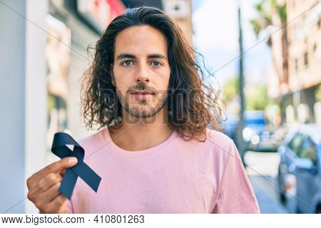 Young hispanic man with serious expression holding mouring black ribbon at city.