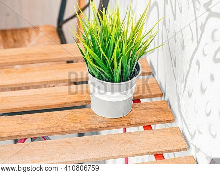 Small Indoor Artificial Flower In White Grey Pot On Wooden Blank Empty Table In Street Cafe