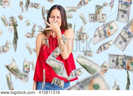 Beautiful brunette young woman wearing casual clothes smelling something stinky and disgusting, intolerable smell, holding breath with fingers on nose. bad smell