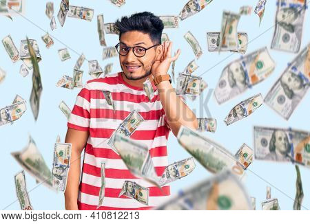 Handsome latin american young man wearing casual clothes and glasses smiling with hand over ear listening an hearing to rumor or gossip. deafness concept.