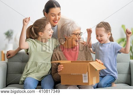 Grandmother, her daughter and granddaughters are unpacking cardboard box at home.