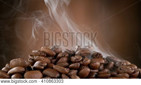 Falling Roasted Coffee Beans on Brown Background, close-up.