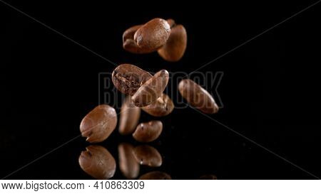 Falling Roasted Coffee Beans on Black Background, close-up.