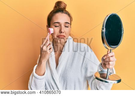Young blonde woman wearing robe holding makeup remover brush depressed and worry for distress, crying angry and afraid. sad expression. 
